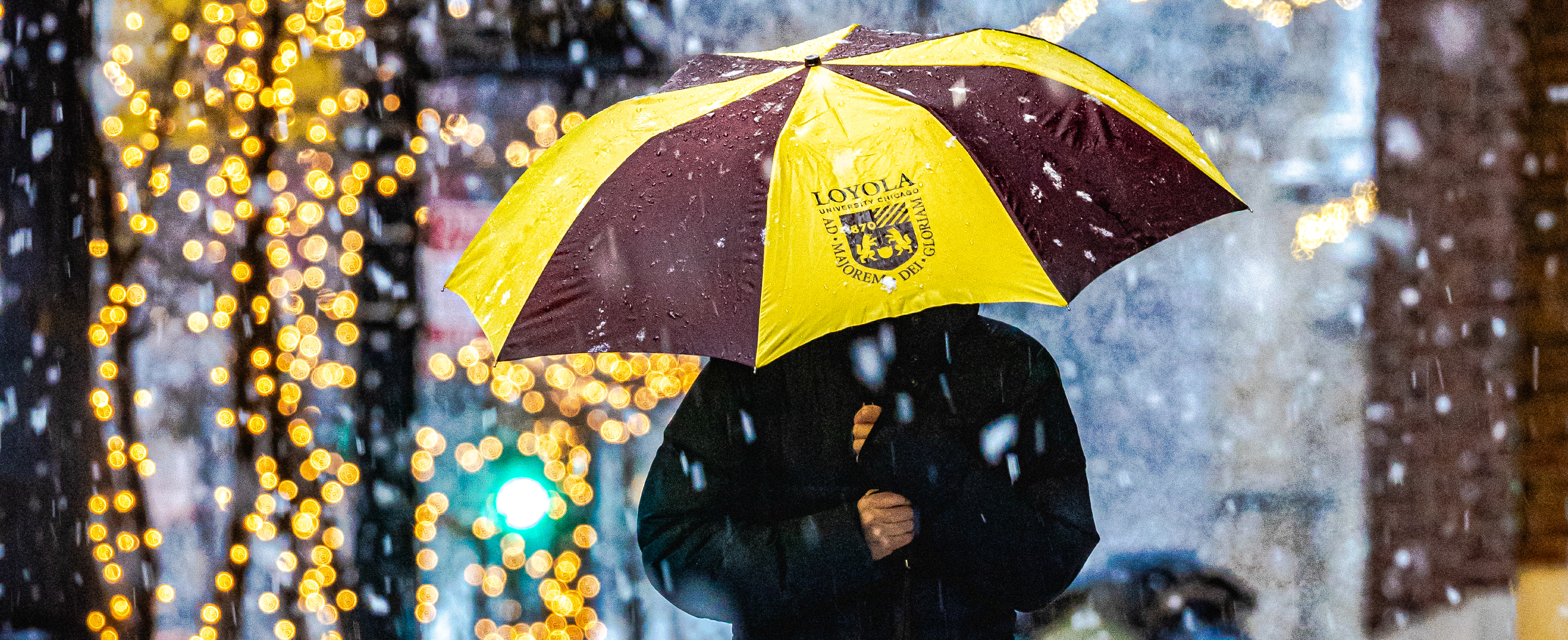 Student sheltering under an umbrella in maroon and gold in the rain